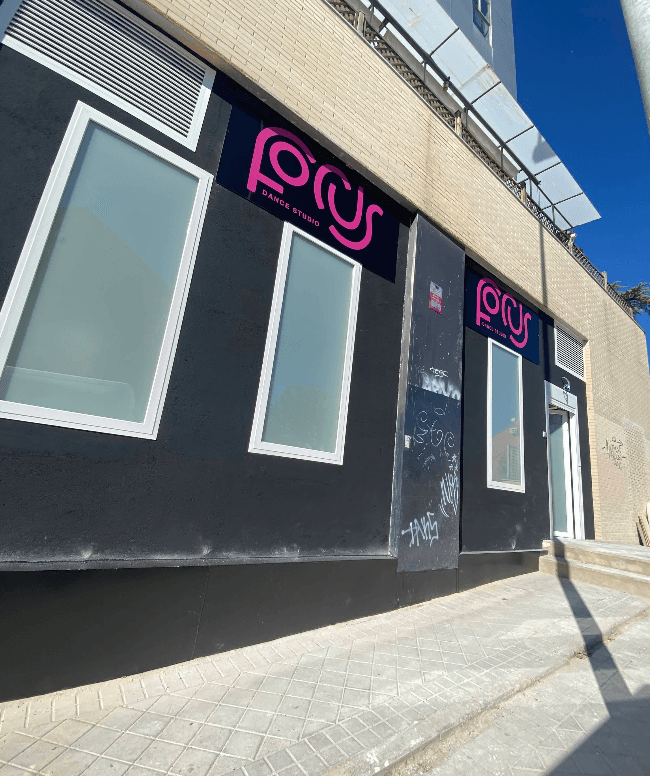 Fachada negra de Focus Dance Studio con logotipos rosa neón y grandes ventanas esmeriladas.